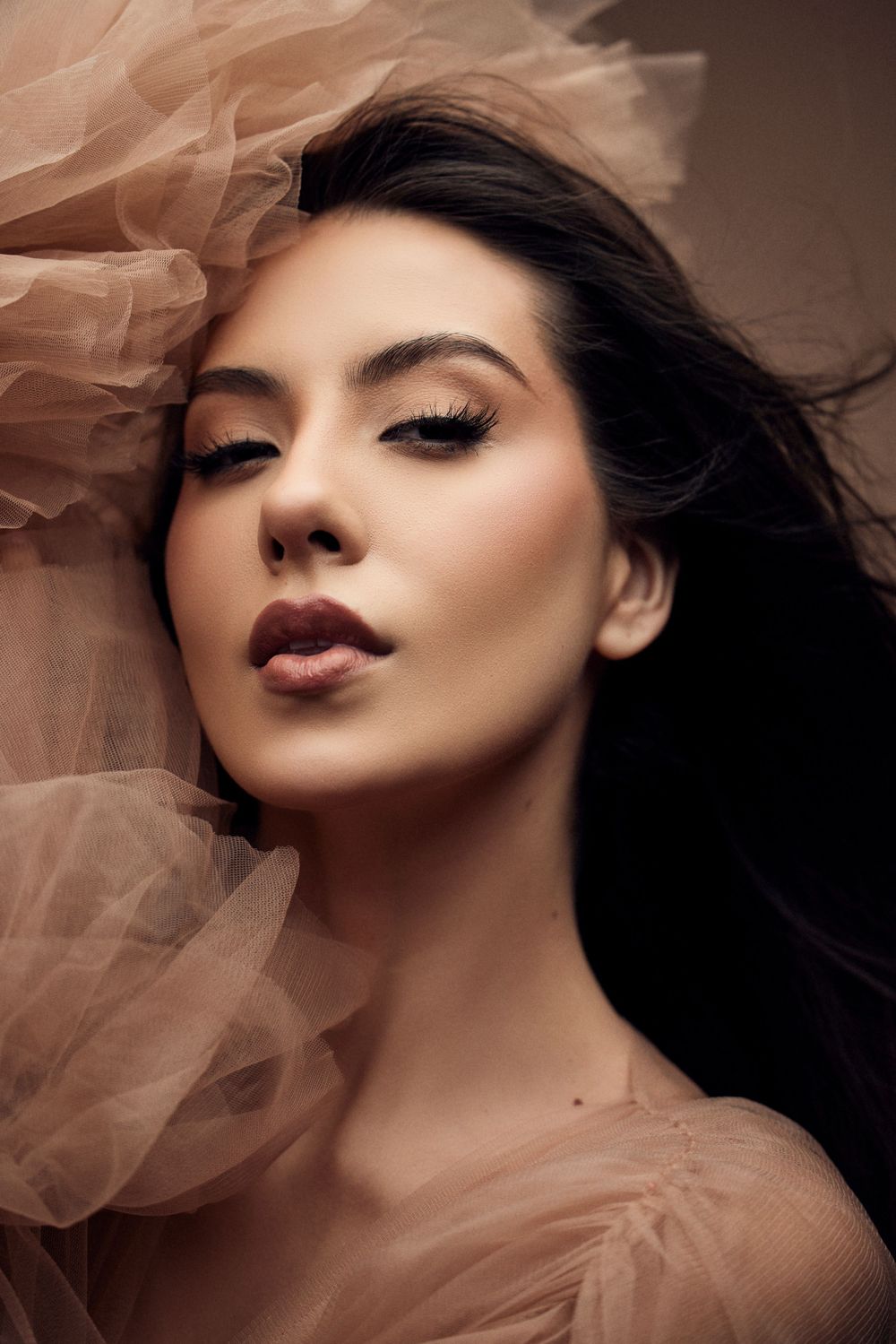 Beauty portrait with soft tulle fabric creating ethereal mood against dark background.