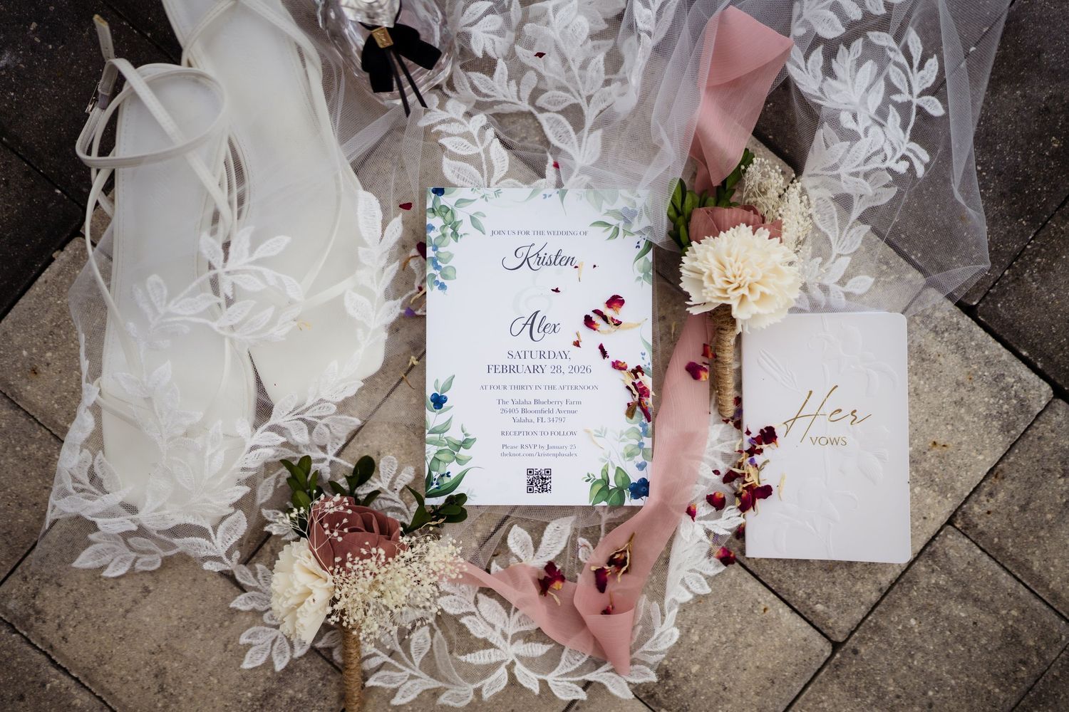 Elegant wedding invitation suite with floral design laid out with delicate fabric and dried flowers on stone surface.