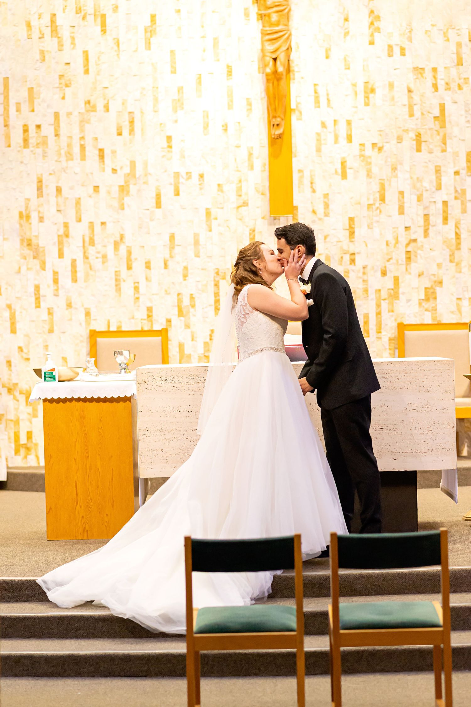 A bride and groom share a romantic kiss at the altar during their wedding ceremony in a modern church setting.