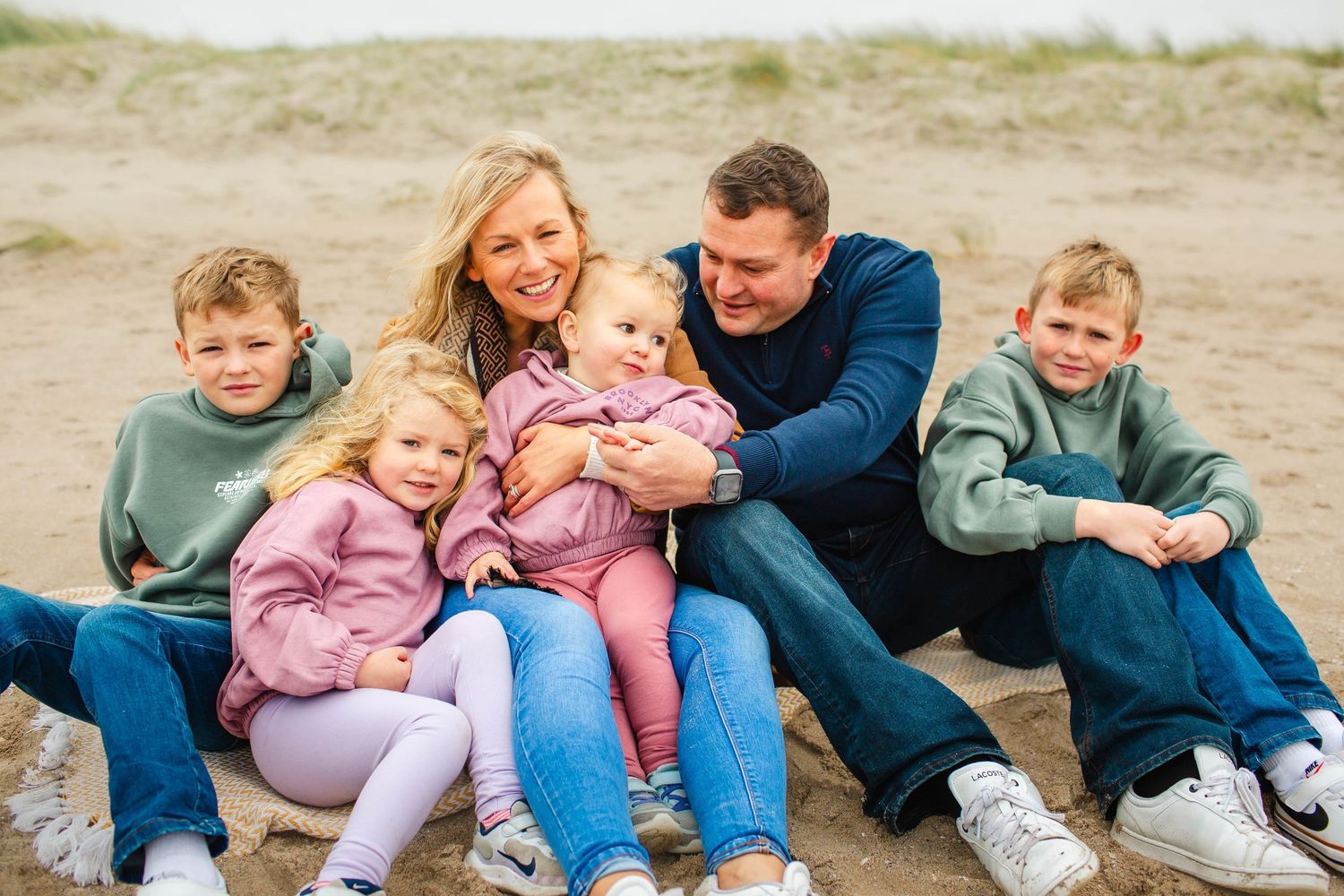 A series of candid family photos taken on a beach with people sitting and laughing together on the sand.