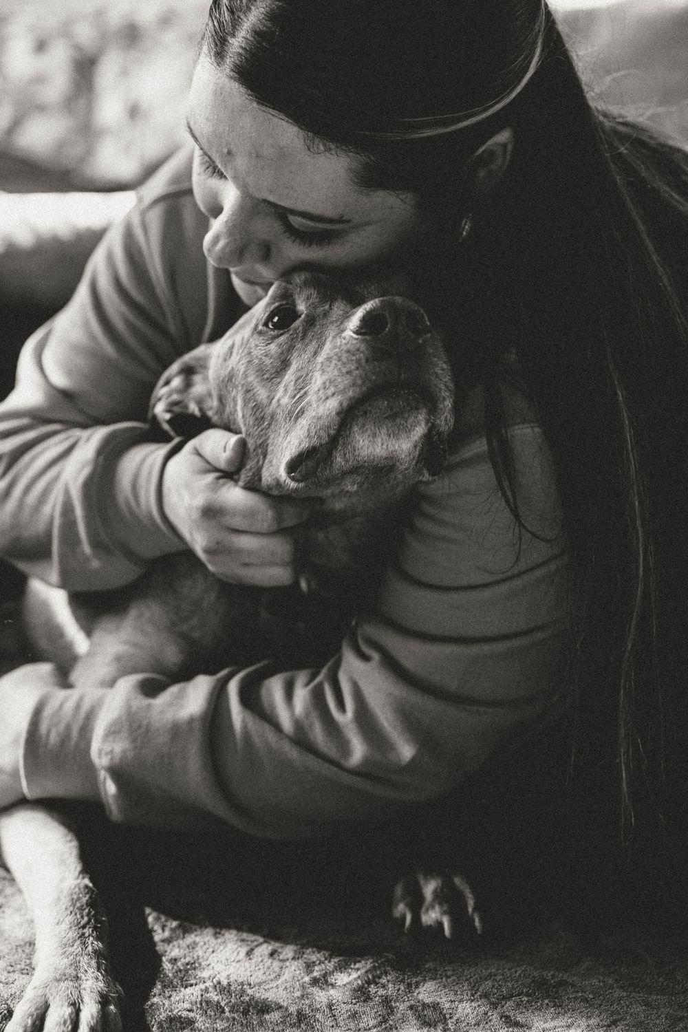 Black and white portrait of person cuddling with their pitbull dog.