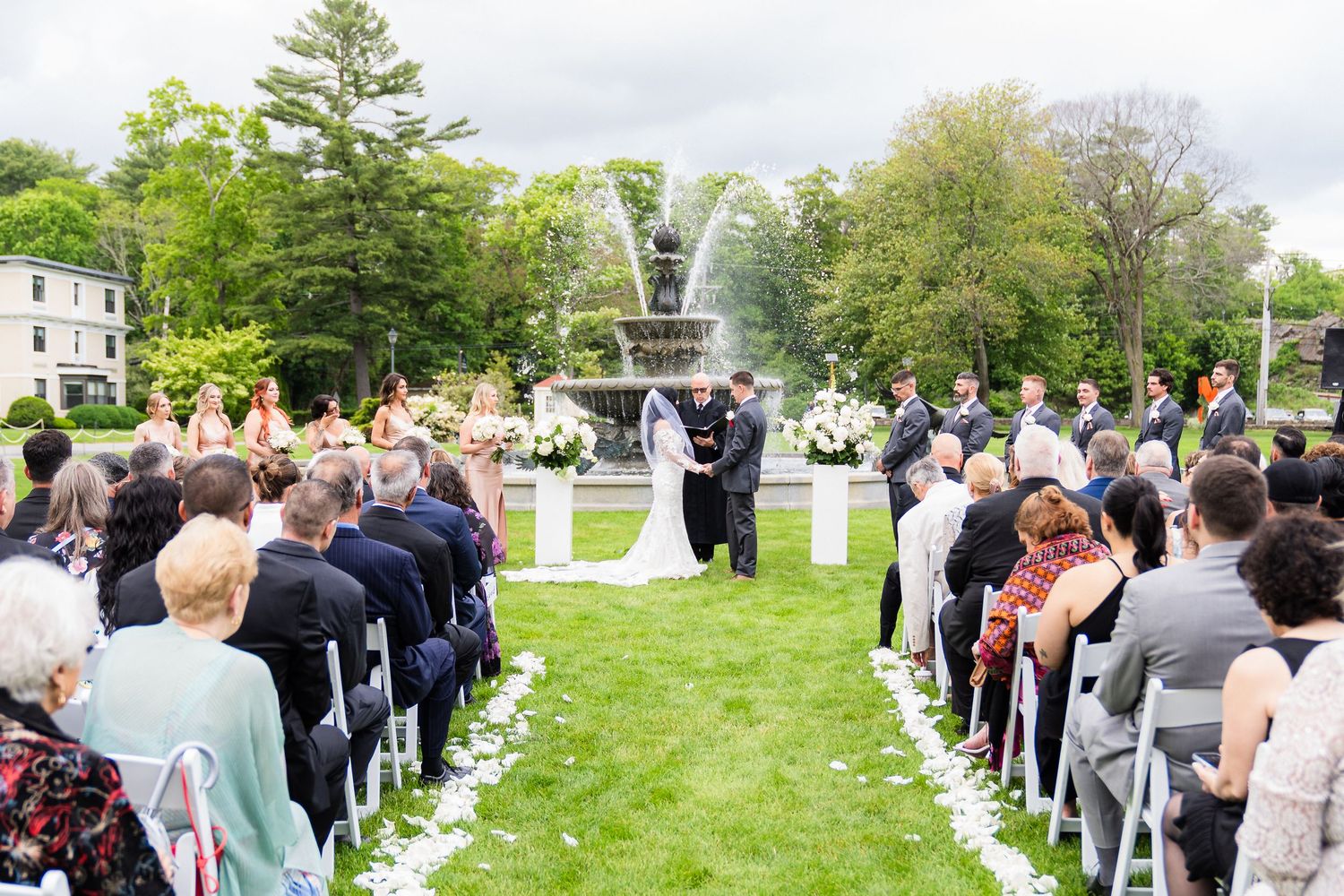 Outdoor wedding ceremony at Tupper Manor in Beverly, MA with guests gathered on a lush green lawn.