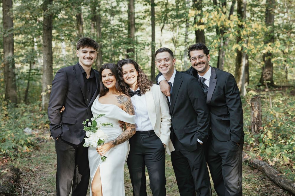 A wedding party poses together in a lush forest setting wearing formal black and white attire.
