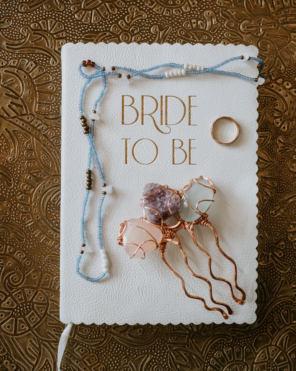 Bride-to-be journal surrounded by crystal hair pins, delicate beaded necklaces, and a gold wedding band.
