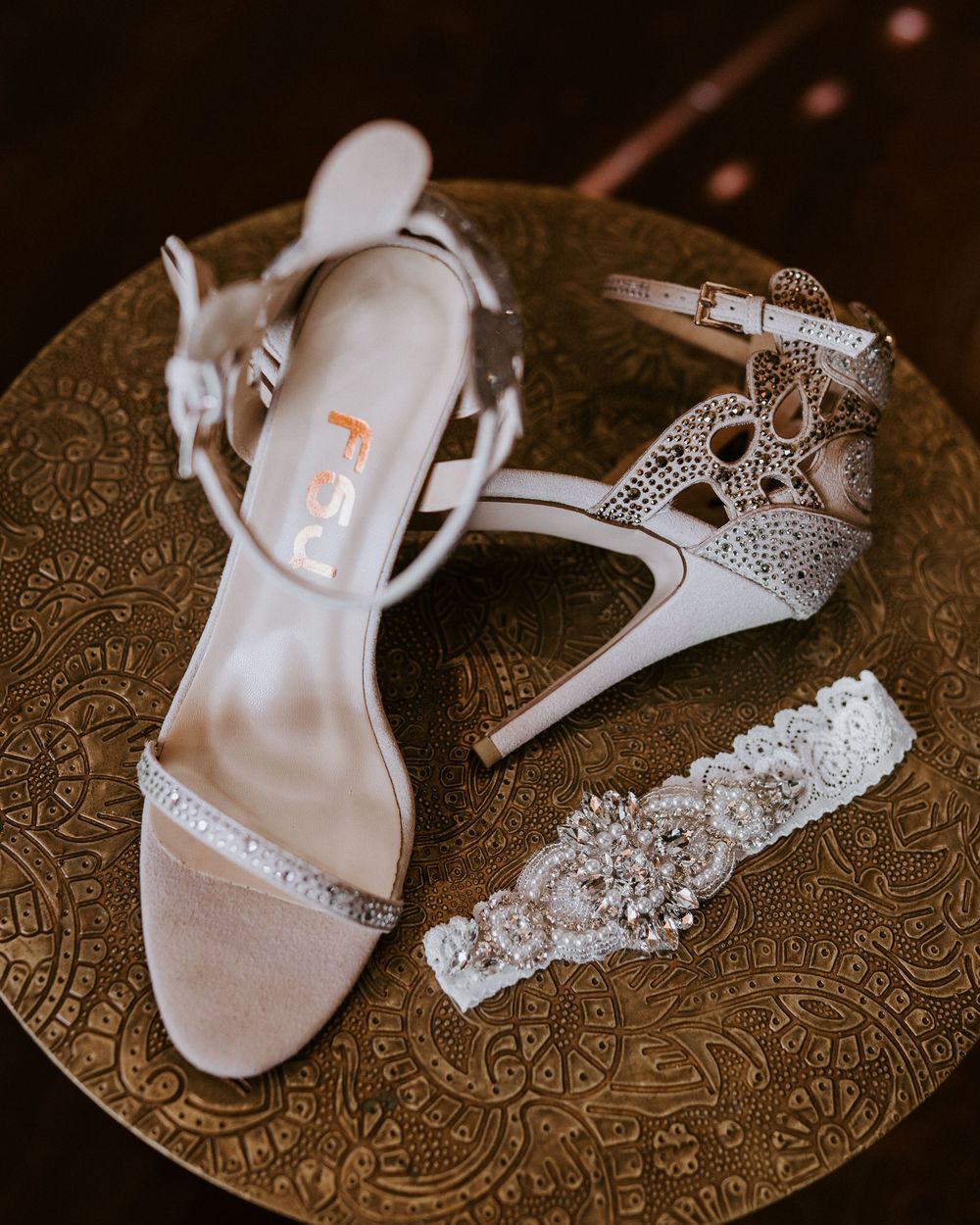 Bridal accessories flat lay featuring strappy heeled shoes, crystal-embellished heels, and a jeweled garter on gold tray.