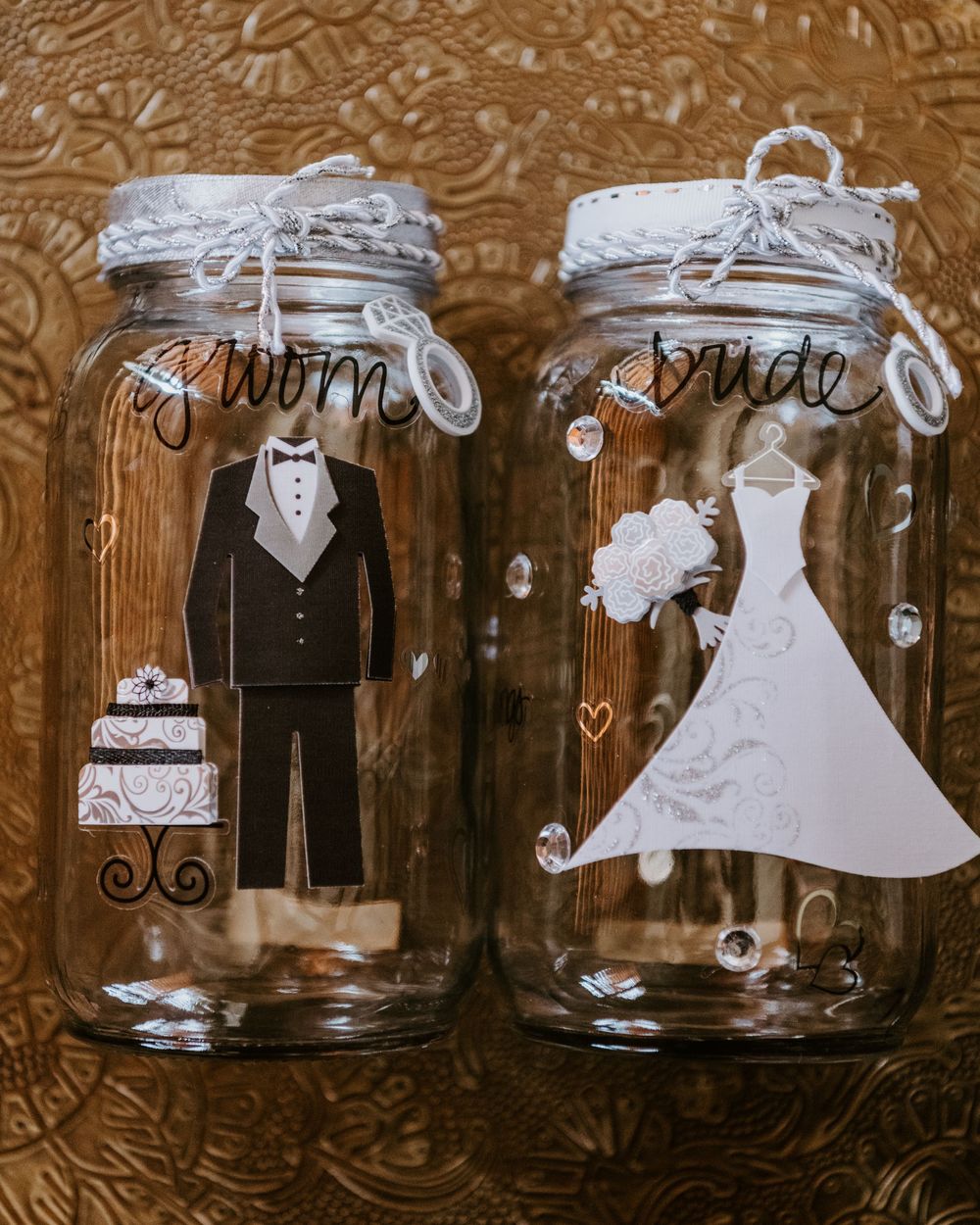 Decorative mason jars labeled bride and groom with illustrated wedding attire designs and heart embellishments.