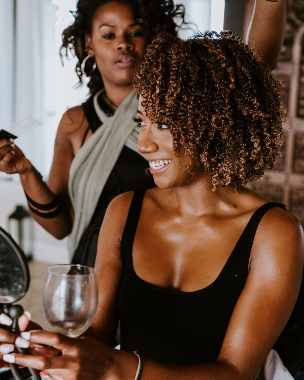 Smiling bride with natural curly hair holding wine glass during bridal getting ready session.