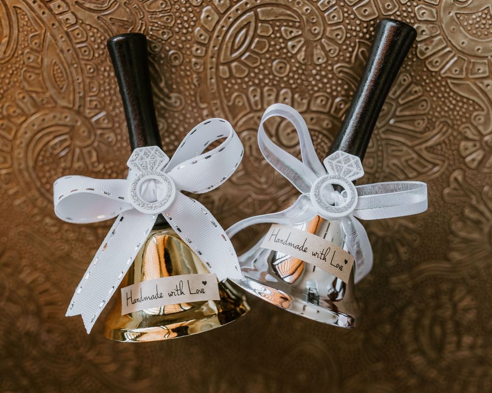 Two decorative wedding bells with white ribbon bows on gold embossed background.