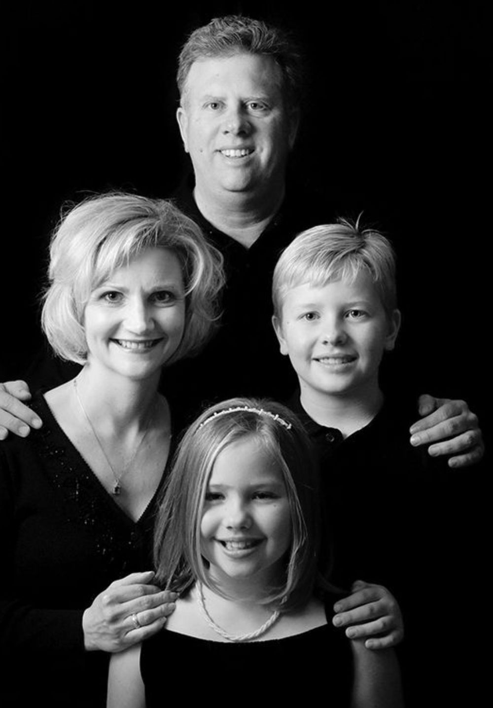A series of black and white family portraits showing intimate moments between parents and children against dark backgrounds.