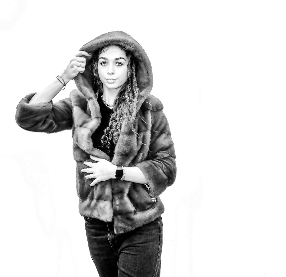 A black and white portrait of someone wearing a fur coat and hat posing against a plain background.