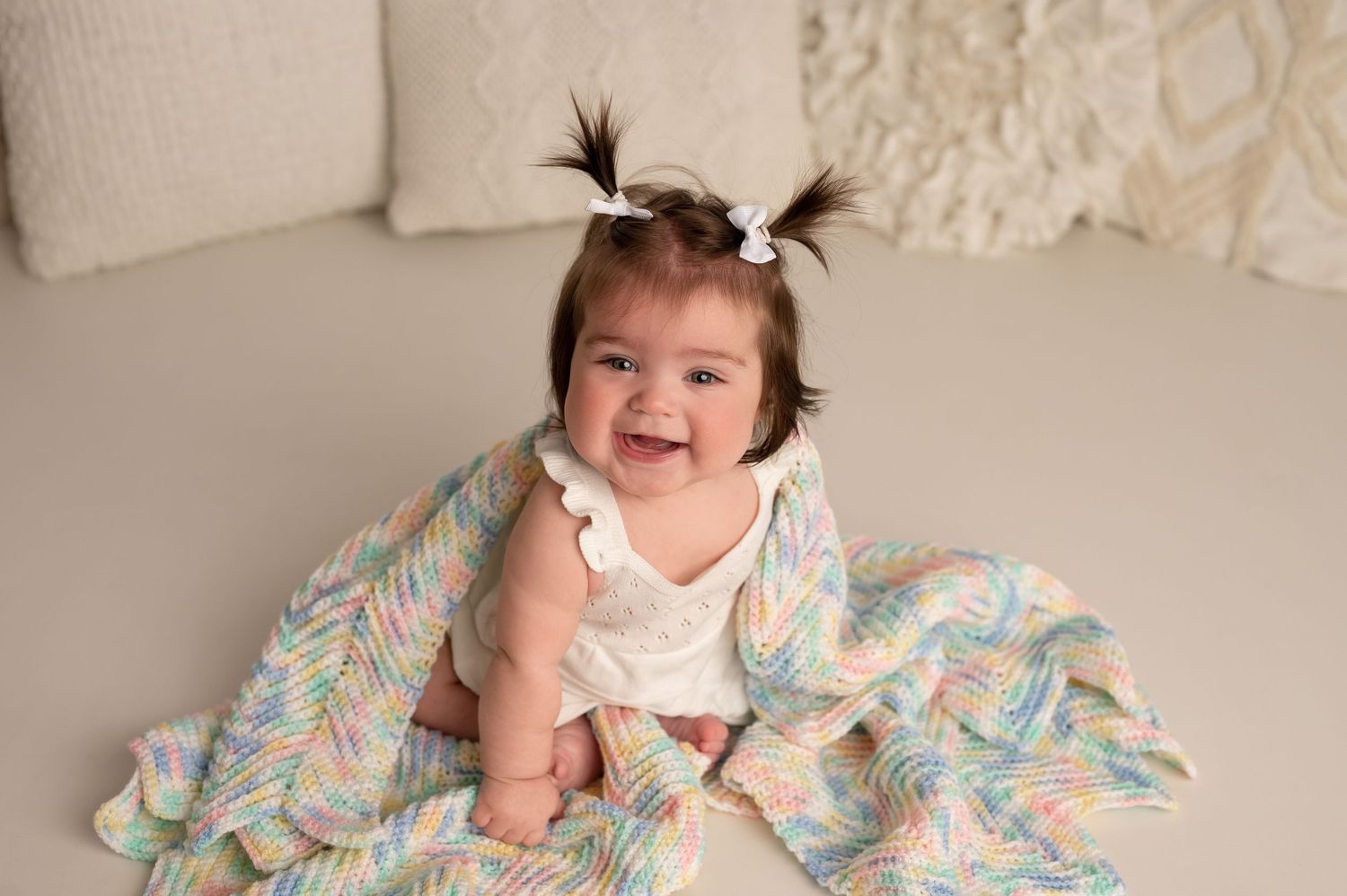 A series of photos showing a baby in a floral dress sitting and smiling on a beige backdrop.