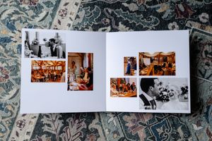 An open photo album displaying vintage black and white and sepia photographs laid on a decorative floral patterned carpet.