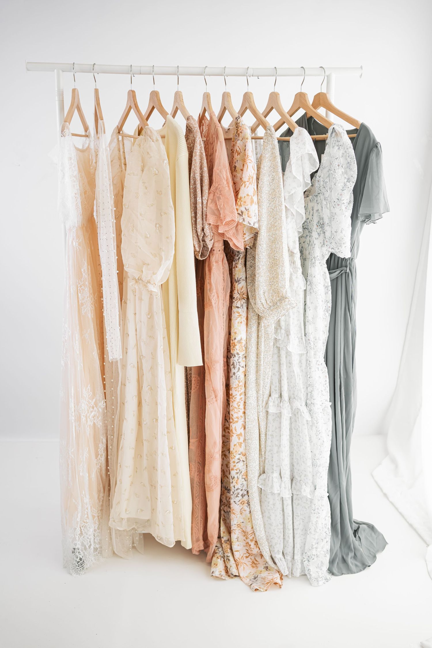 Elegant collection of pastel and neutral colored dresses hanging on white hangers against a white background.