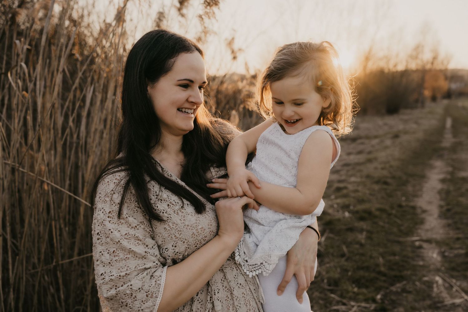 Mother and daughter share tender moments during sunset photoshoot in rustic outdoor setting.