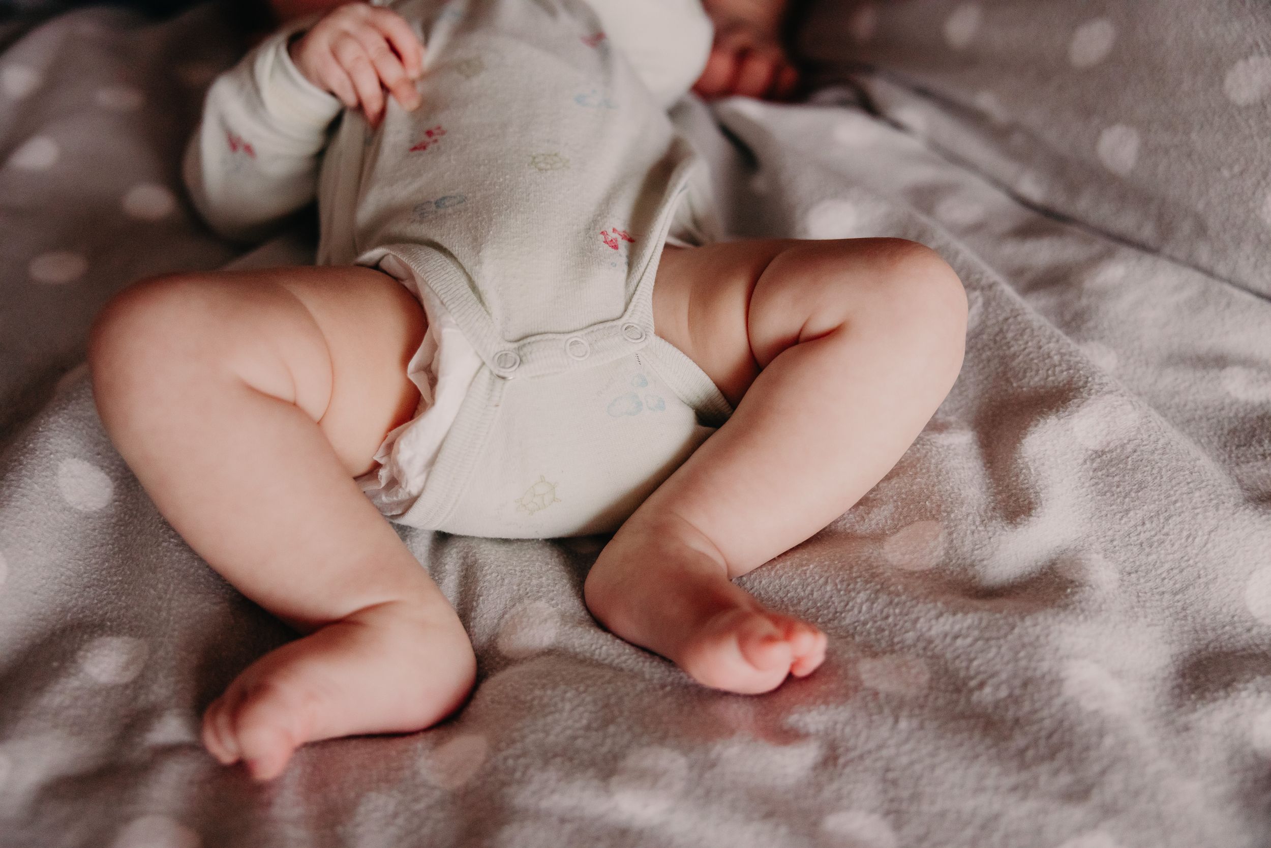 Close-up of chubby newborn baby legs and feet on gray blanket.