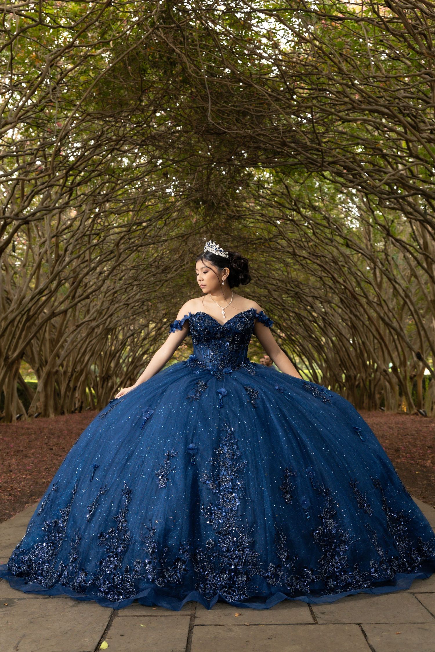 Expectant woman in flowing mauve gown and floral crown poses elegantly against neutral backdrop in maternity photo.