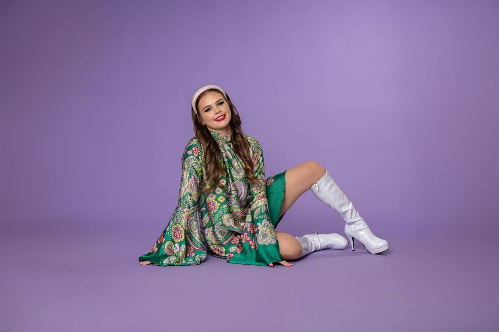 Fashion model in green floral dress and white boots poses on purple background in multiple dynamic poses.