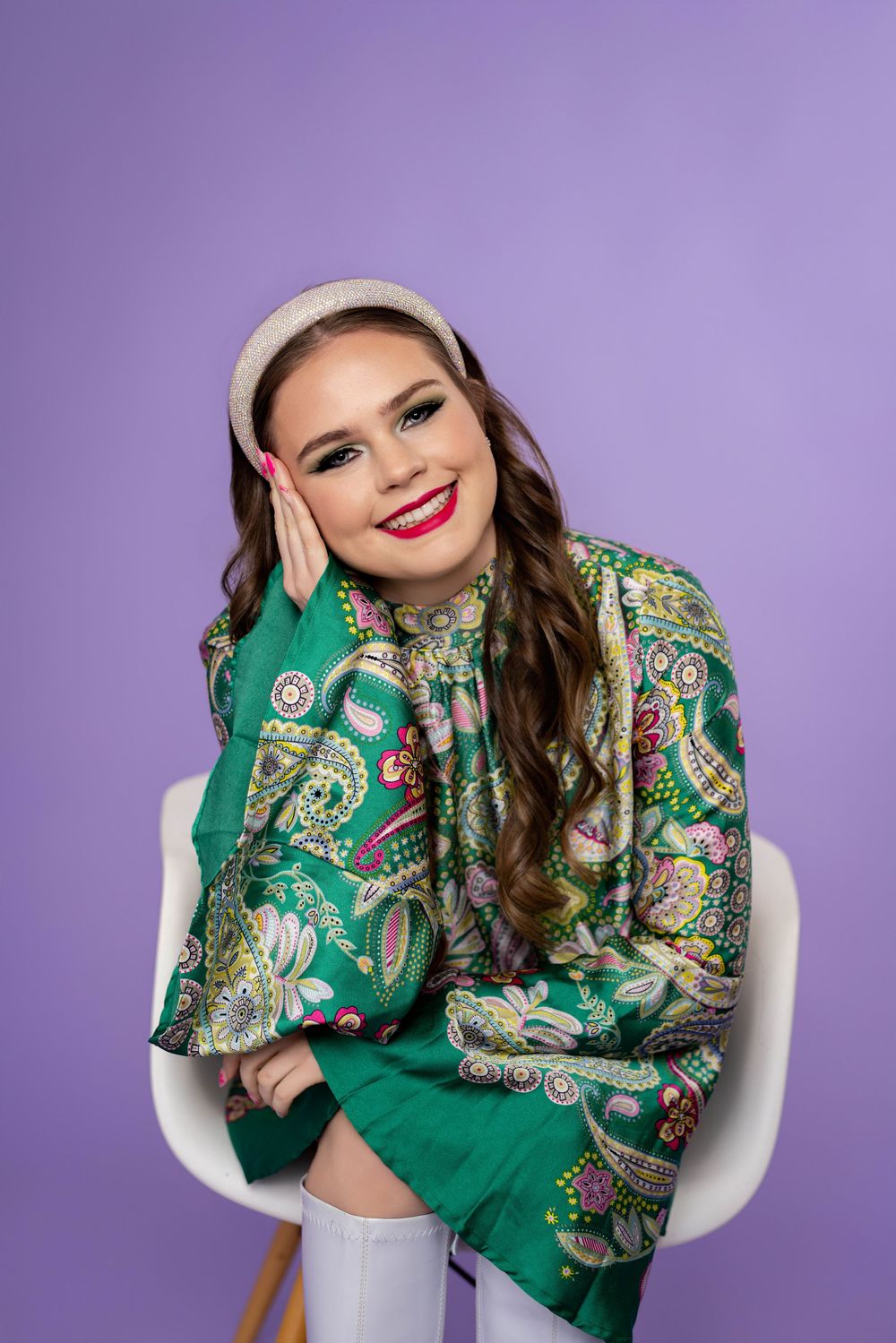 Fashion portrait featuring emerald paisley print garment and white headband against purple studio backdrop.