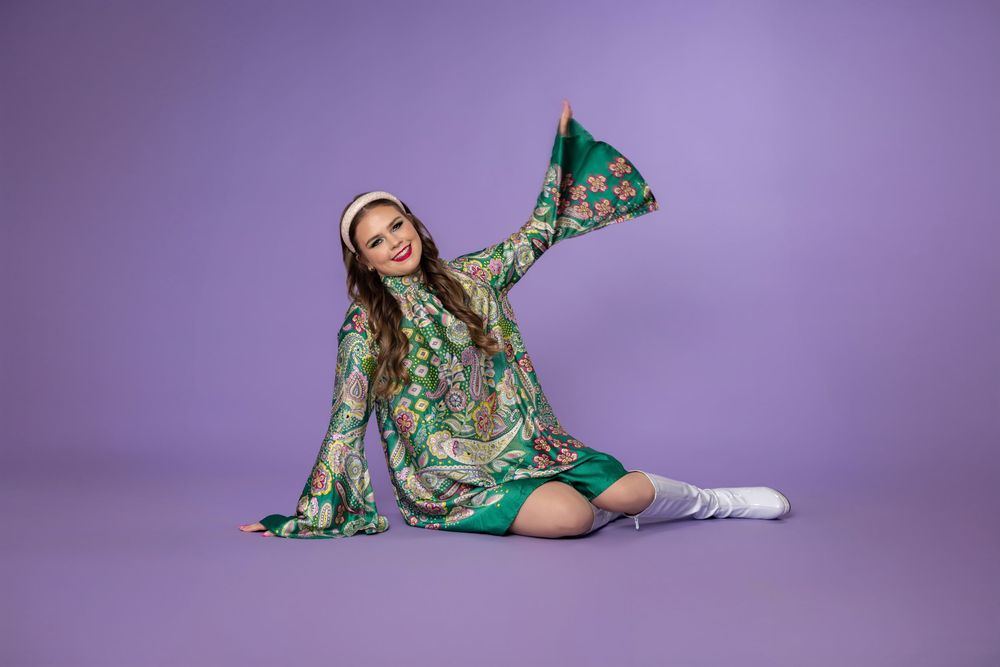 Model in green floral print dress poses dynamically against purple backdrop in fashion photography series.
