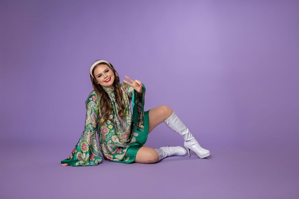 A person in a green sequined dress and white boots poses in various positions against a purple backdrop.
