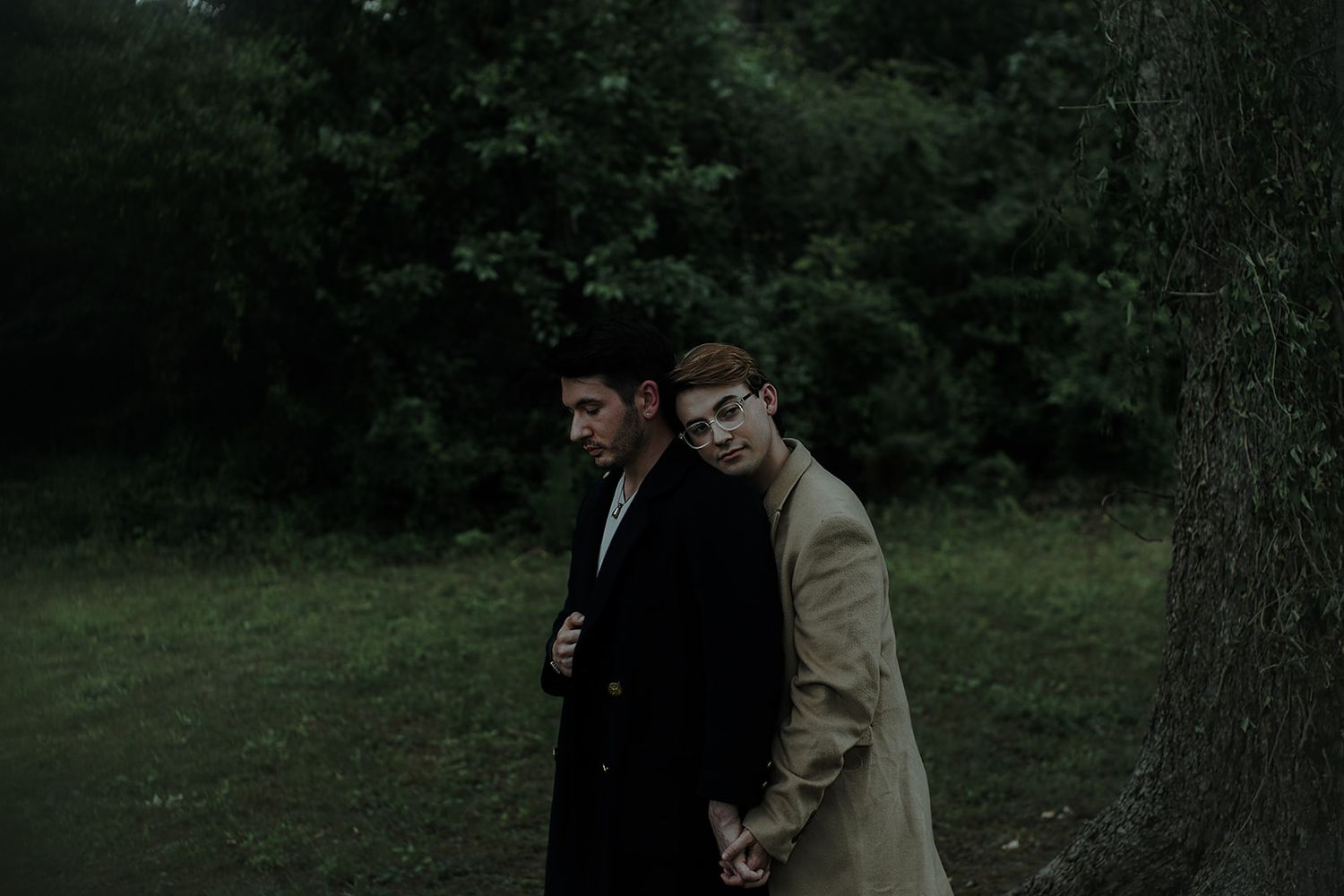 Two figures share an intimate moment in a dark wooded setting.
