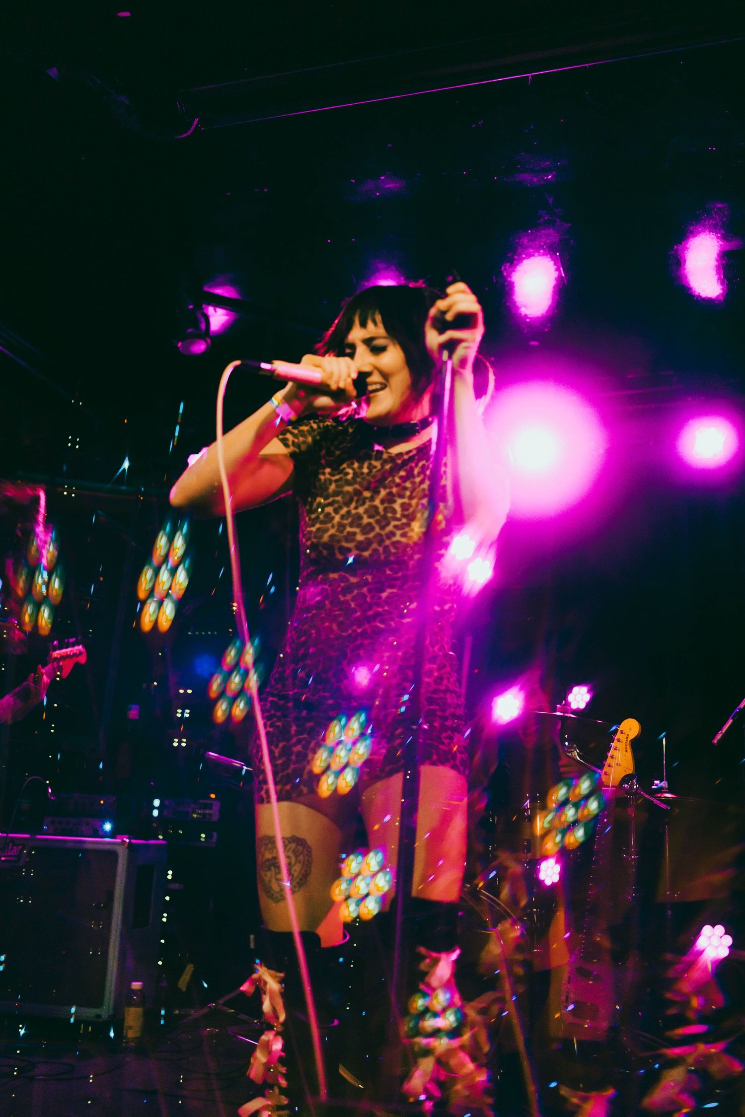 Concert performer singing on stage with vibrant pink and purple lighting effects.