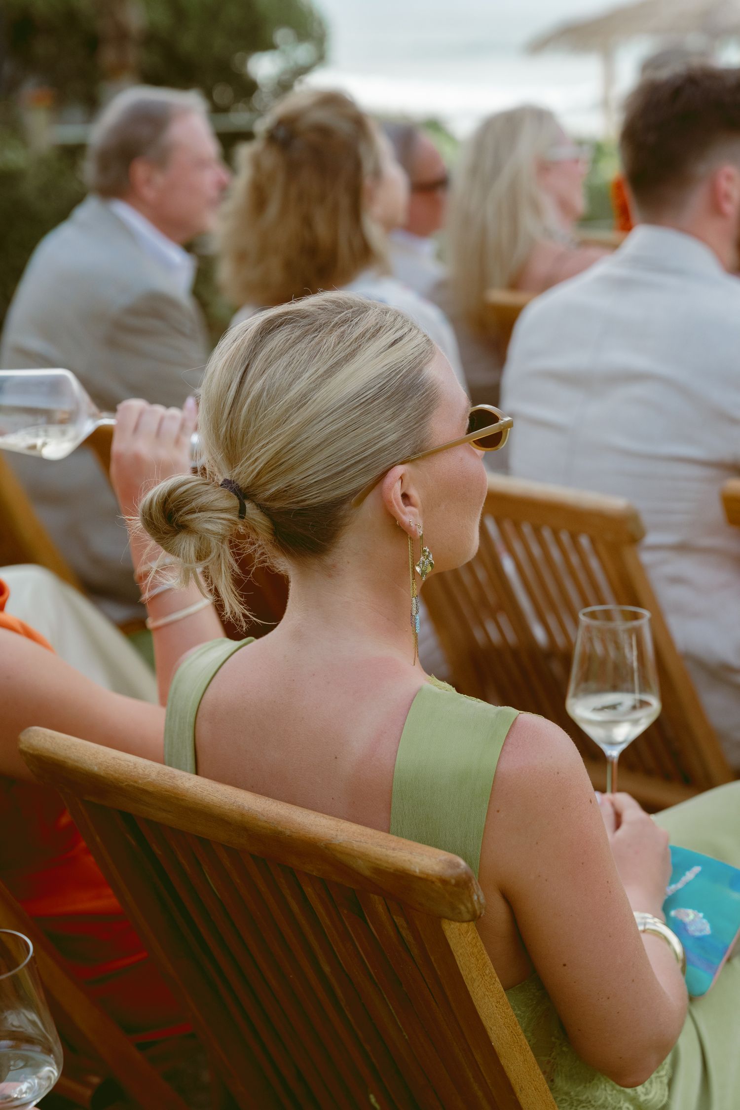Guest in mint green dress enjoying outdoor wedding reception with wine glass.