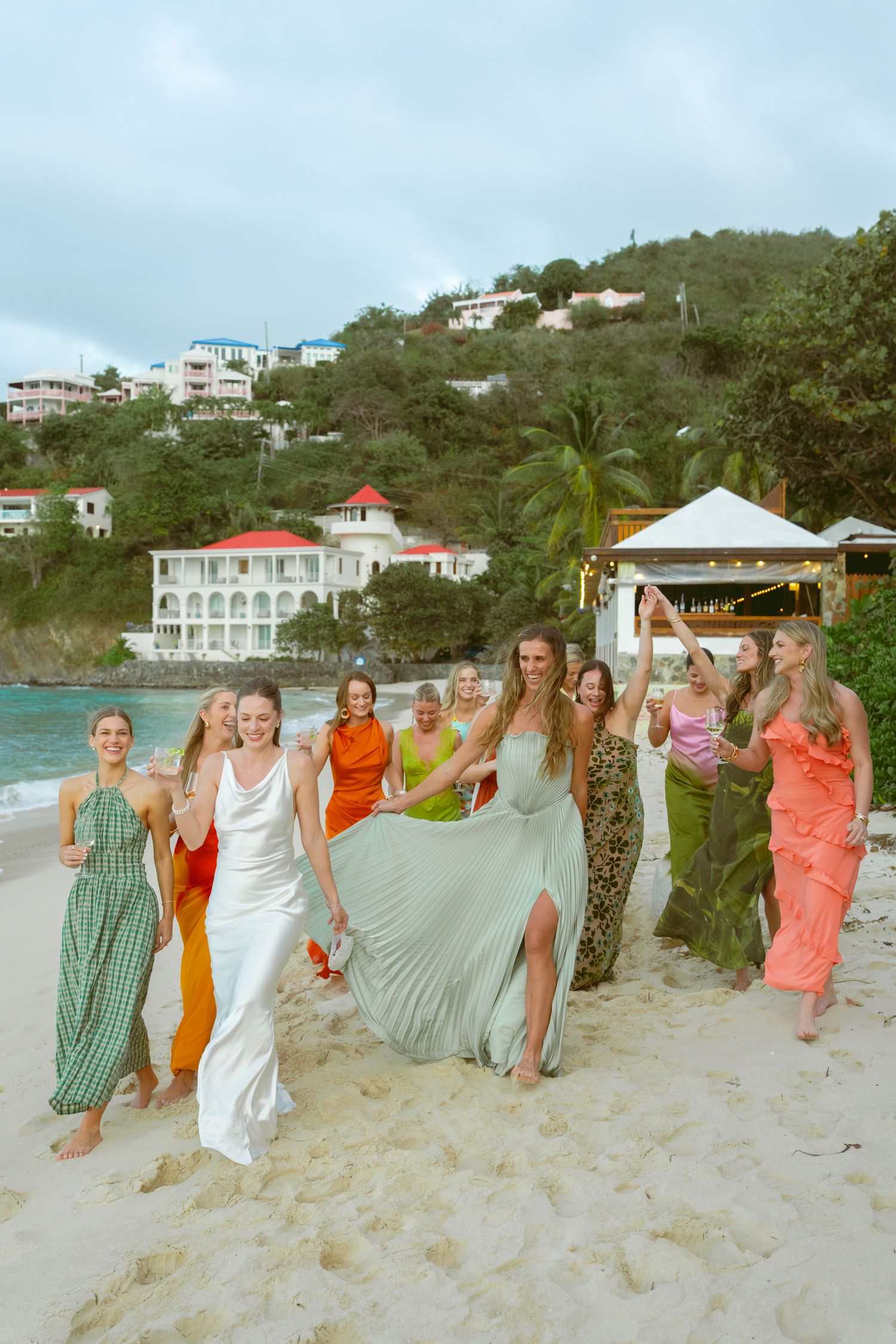 Wedding party walking together on a scenic beach with coastal homes in the background.