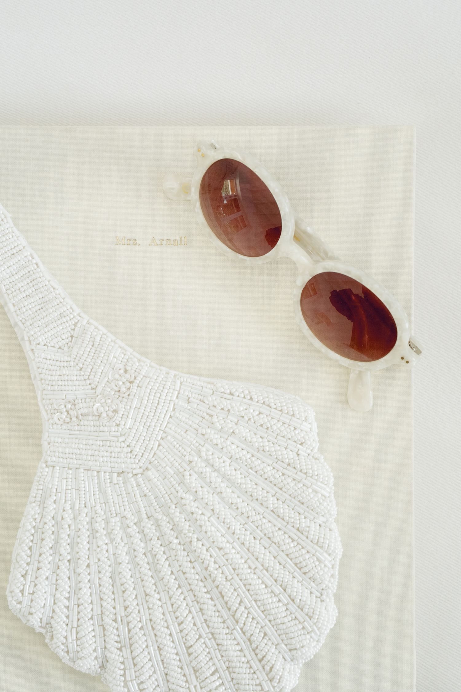 White beaded swimsuit top and retro sunglasses arranged on light background.