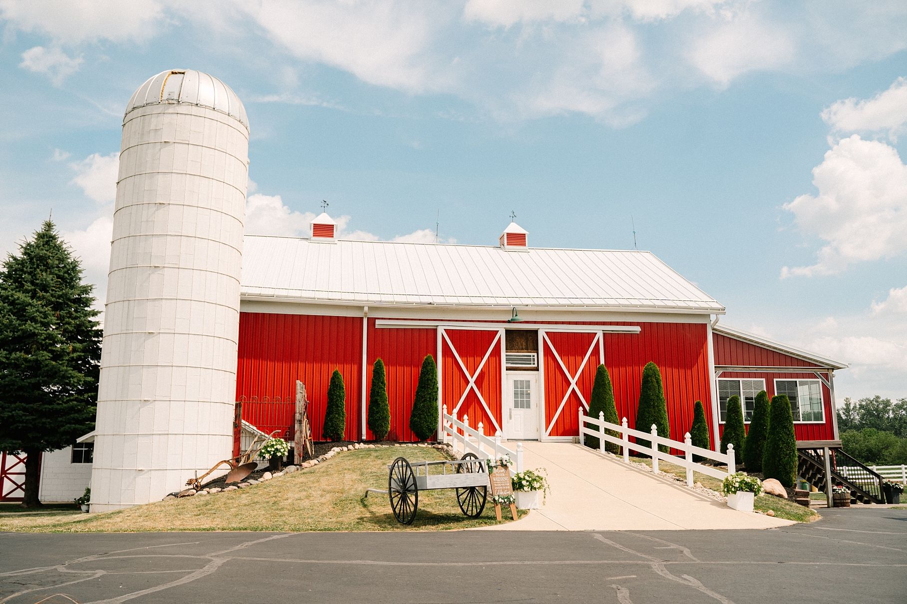 Classic red barn wedding venue with white silo and vintage wagon wheel decor.