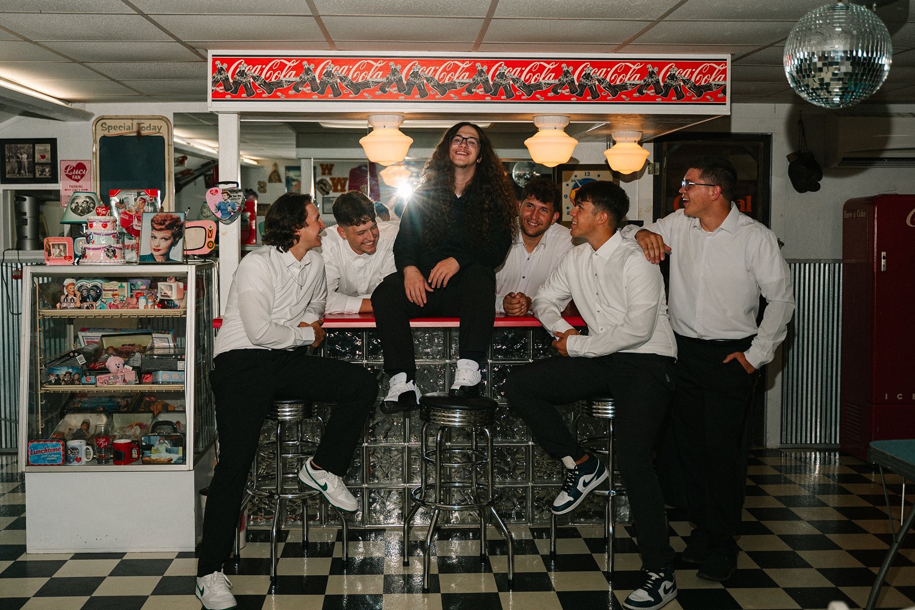 Group of young men gather around a bar counter in a vintage Coca-Cola themed diner.