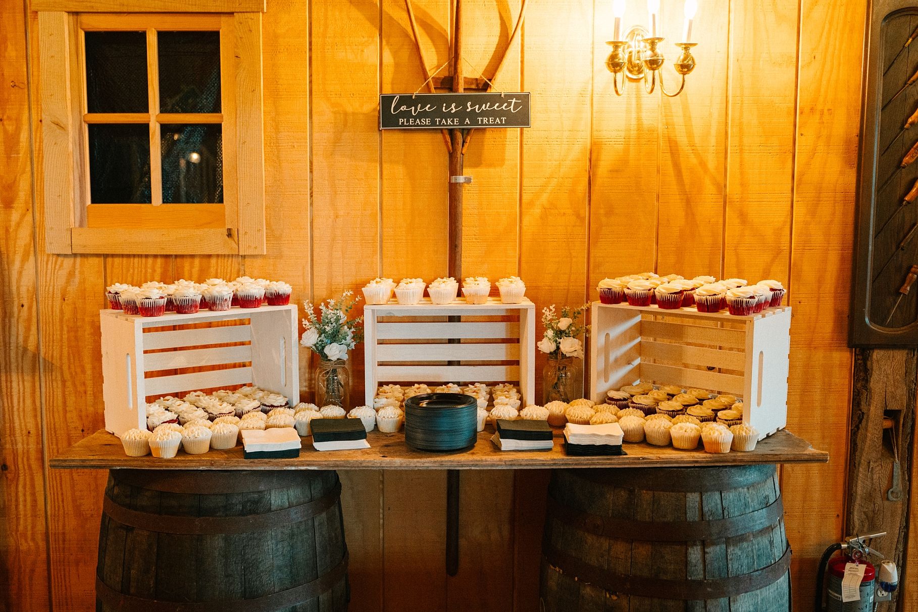 Rustic wedding dessert table with cupcakes displayed on white crates atop wooden barrels.