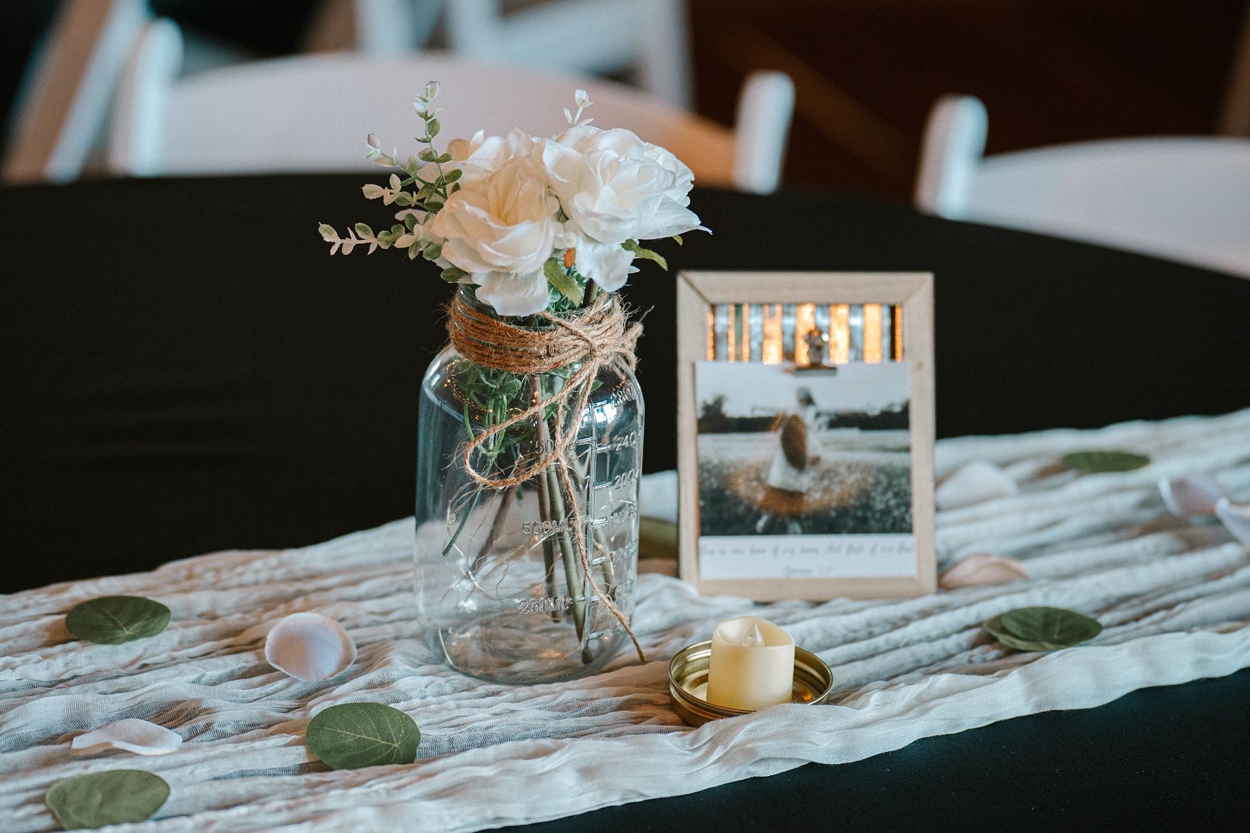 Elegant wedding centerpiece with white roses in a mason jar on a lace table runner.