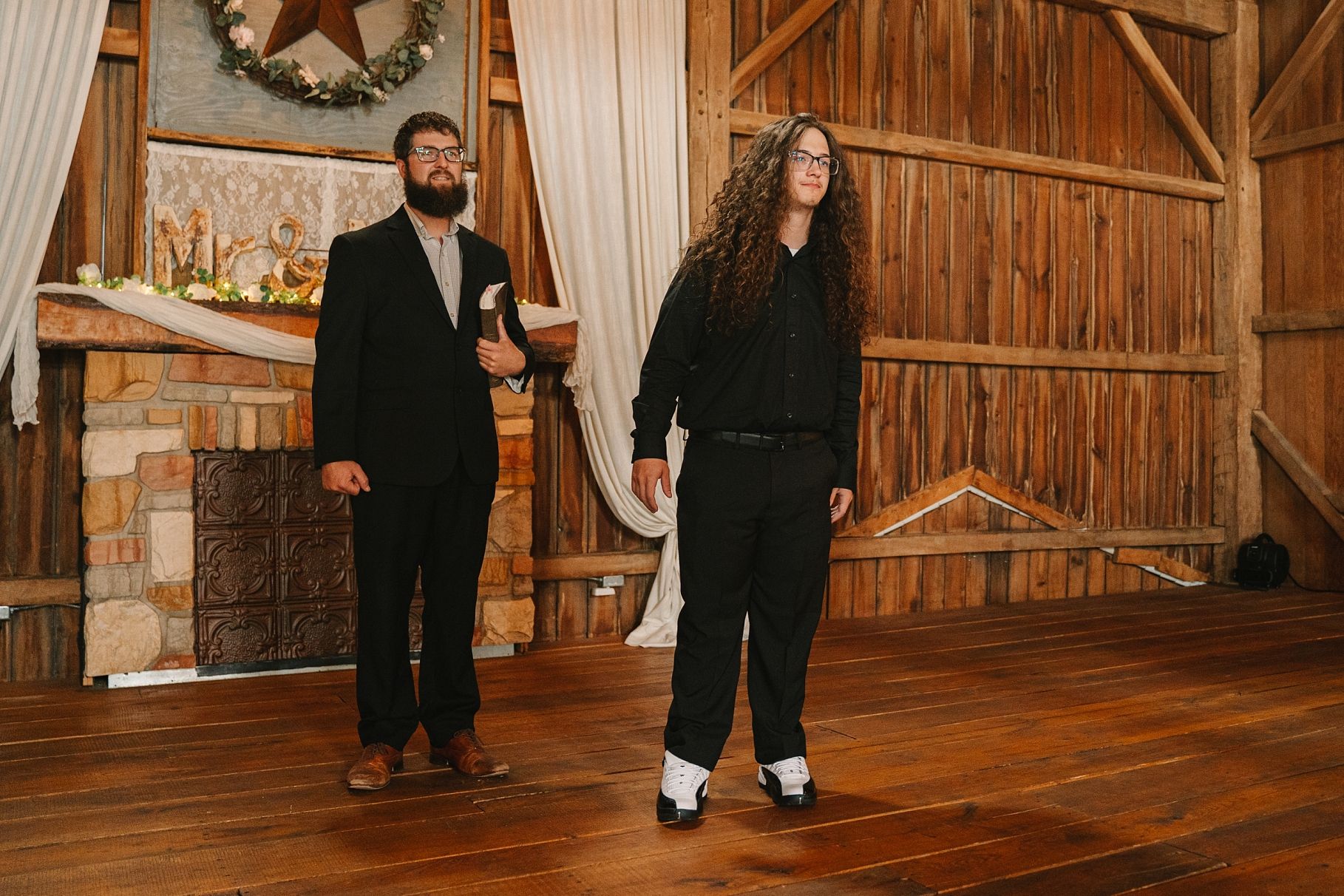 Bride and groom stand in a rustic barn wedding venue with wooden walls and fireplace.