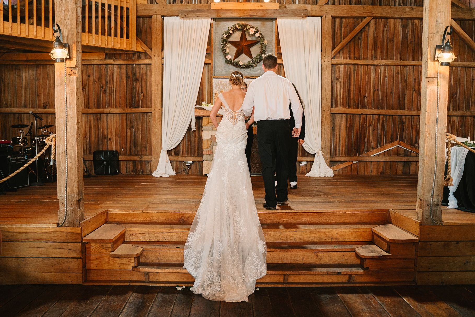 Bride and groom walk toward altar in a warmly lit rustic barn wedding ceremony.