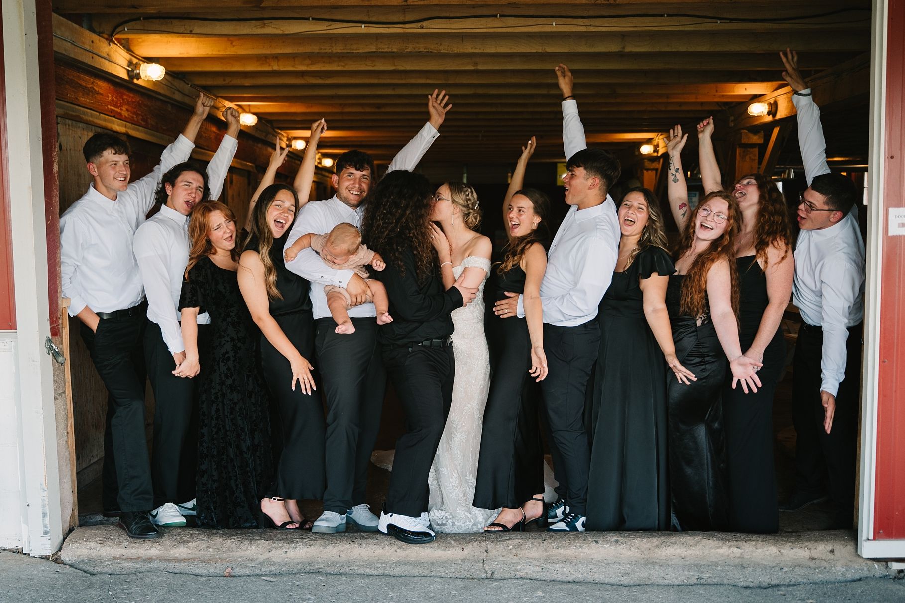 Wedding party celebrating in doorway of rustic barn with arms raised in joyful group photo.