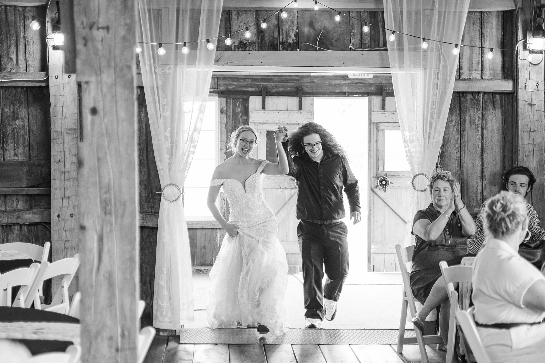 Bride and wedding coordinator walk through rustic barn reception venue in black and white photo.