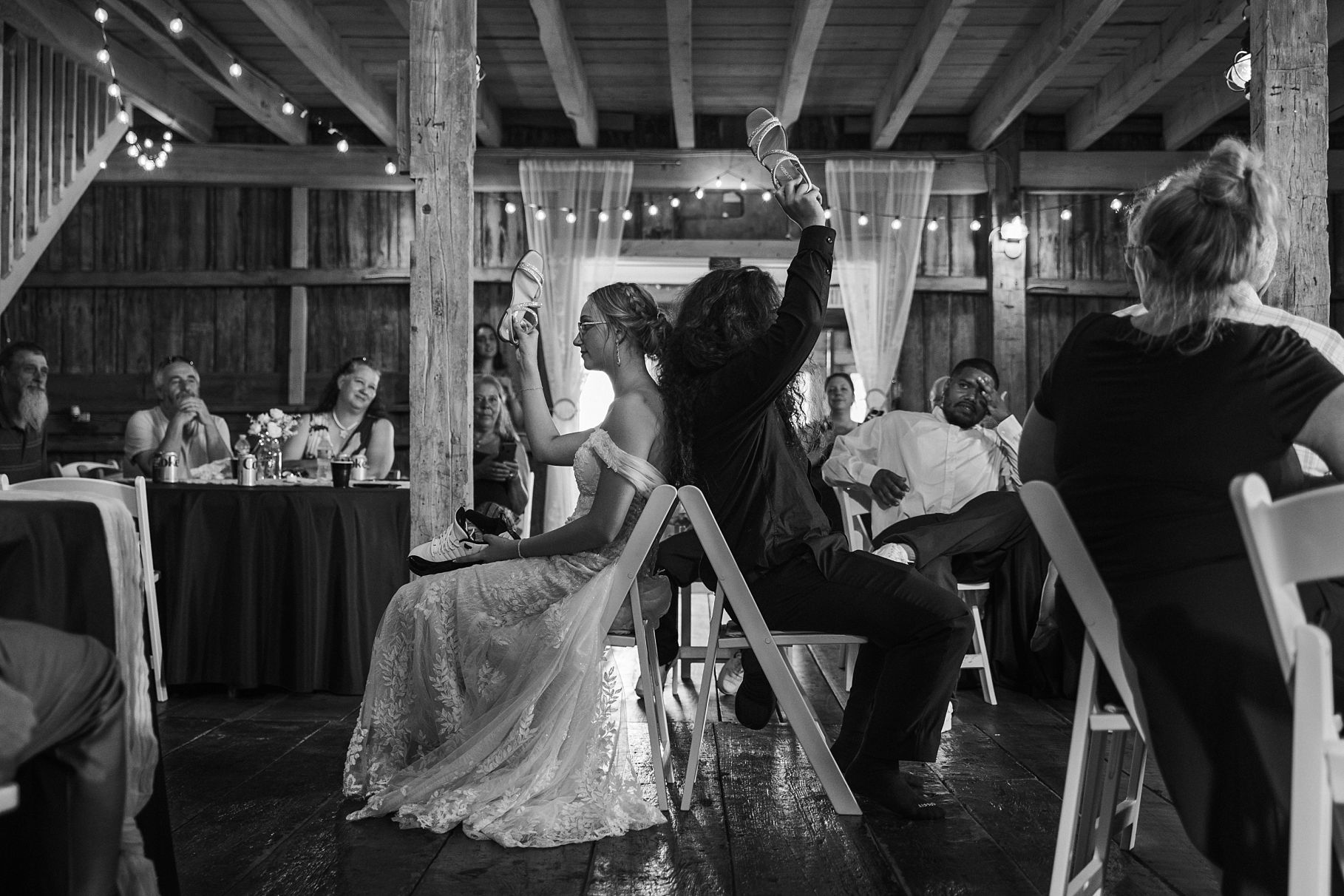 Bride and partner raise glasses during wedding reception toast in black and white barn photo.