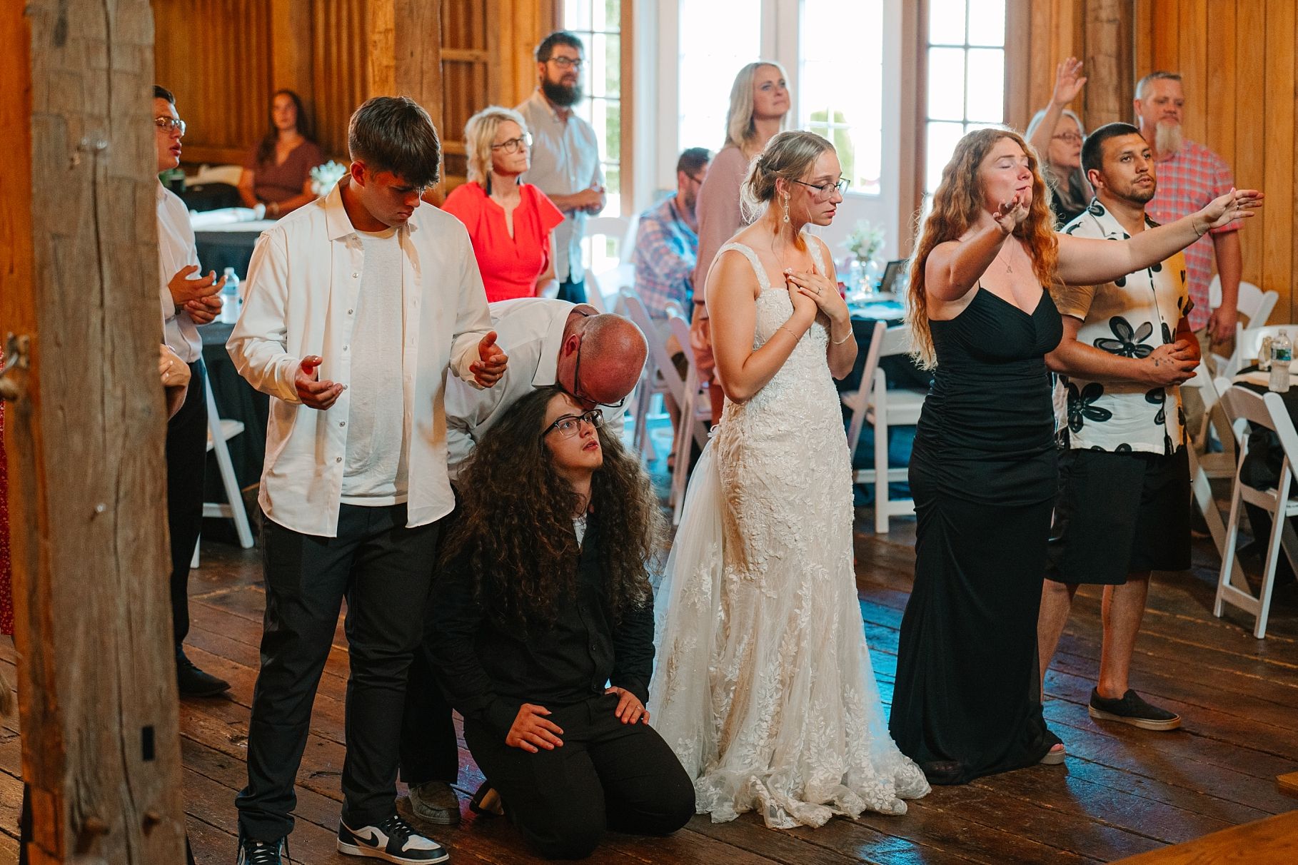 Wedding guests and bride dance together on rustic barn reception venue dance floor.