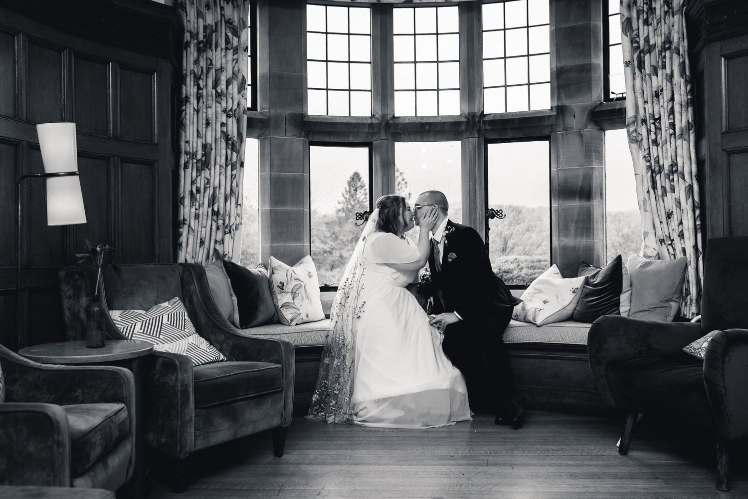 A romantic black and white photo series of a couple in vintage wedding attire sitting in a sunlit window alcove at Cragwood.