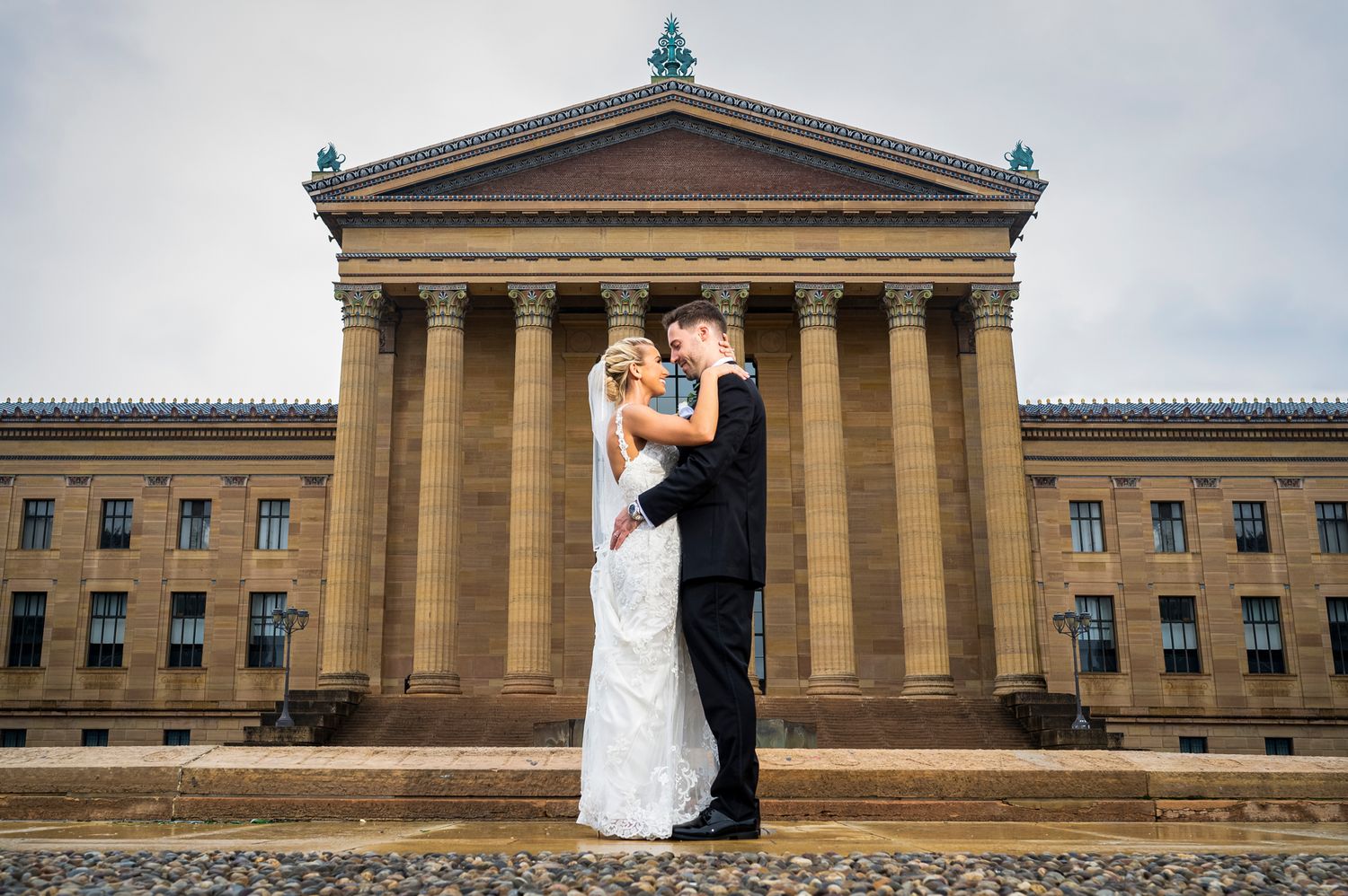 A couple shares a romantic moment on their wedding day in front of the Philadelphia Museum of Art's grand neoclassical facade.