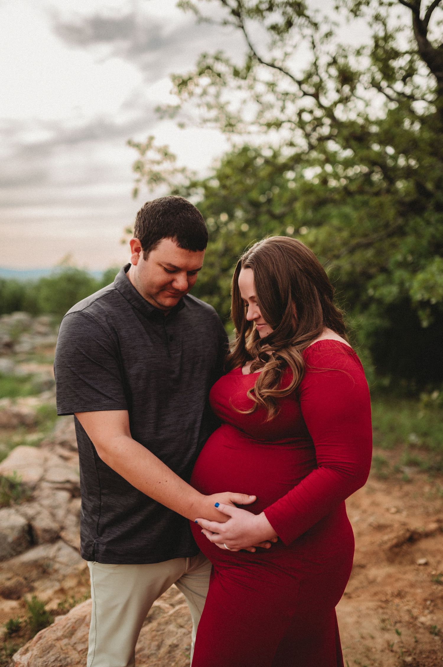 A couple in a grey shirt and red dress share intimate moments outdoors during a golden hour photoshoot.