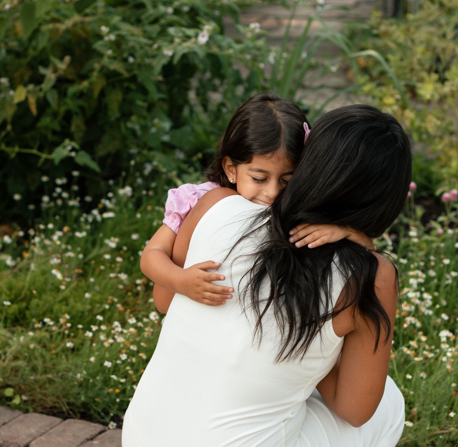A series of tender hugging moments captured in a garden setting with white clothing and natural greenery.