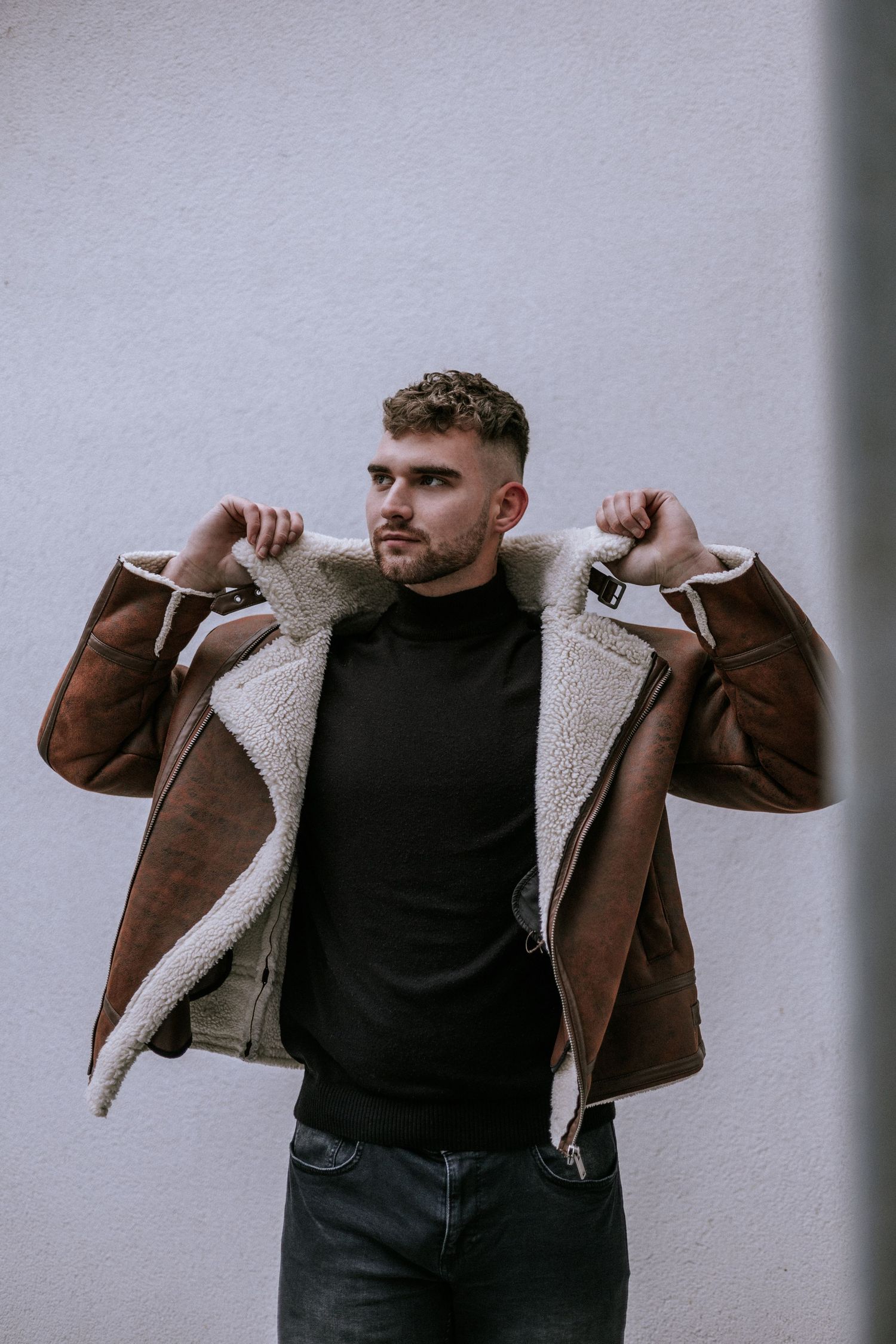 Portrét muža v módnej bunde s bielym barančekom pred minimalistickou stenou. Profesionálne lifestyle a fashion fotenie, Žilinský kraj.