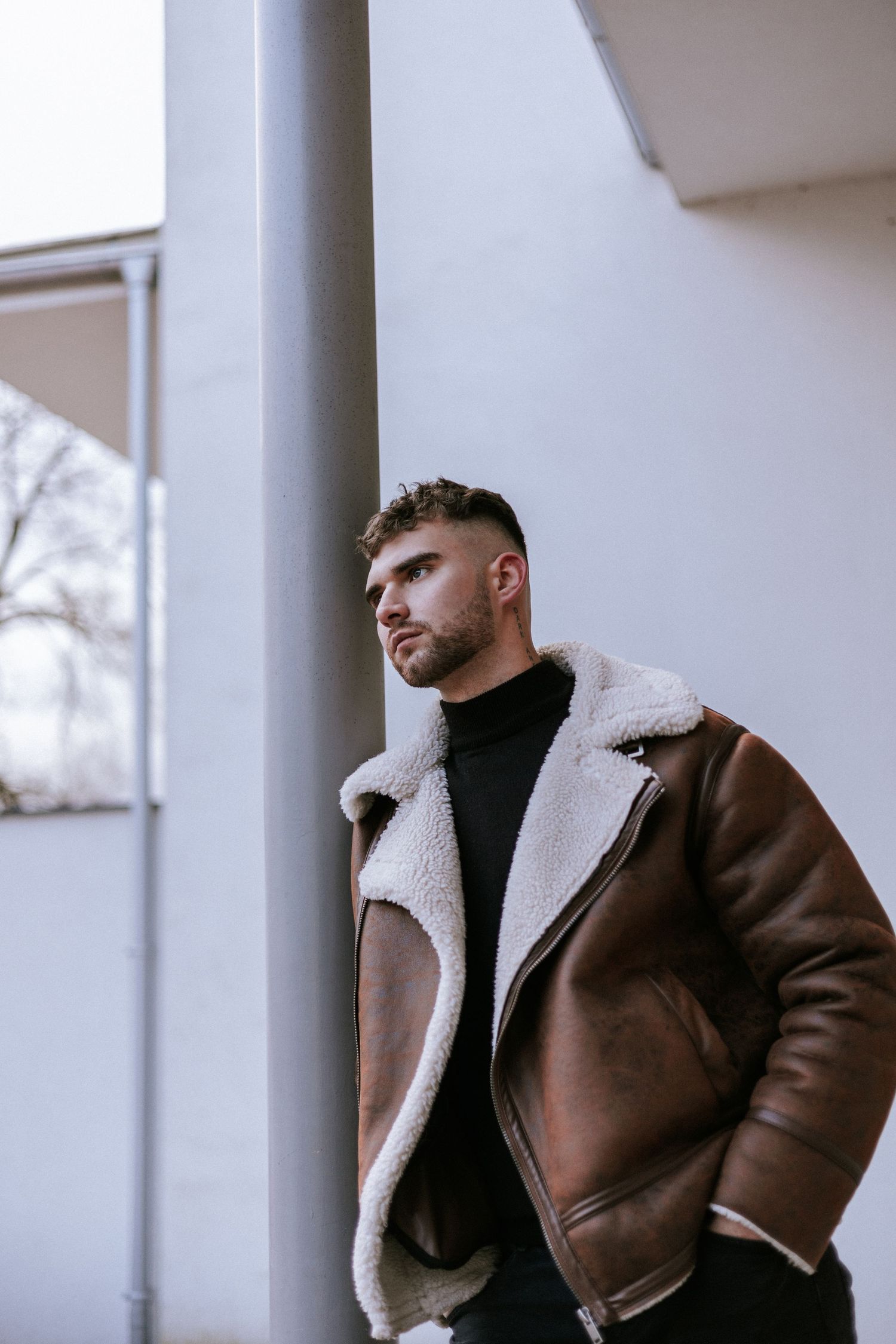 Mladý muž v hnedej koženej bunde pózuje v modernom mestskom prostredí. Profesionálny mužský portrét a street style, Žilinský kraj.