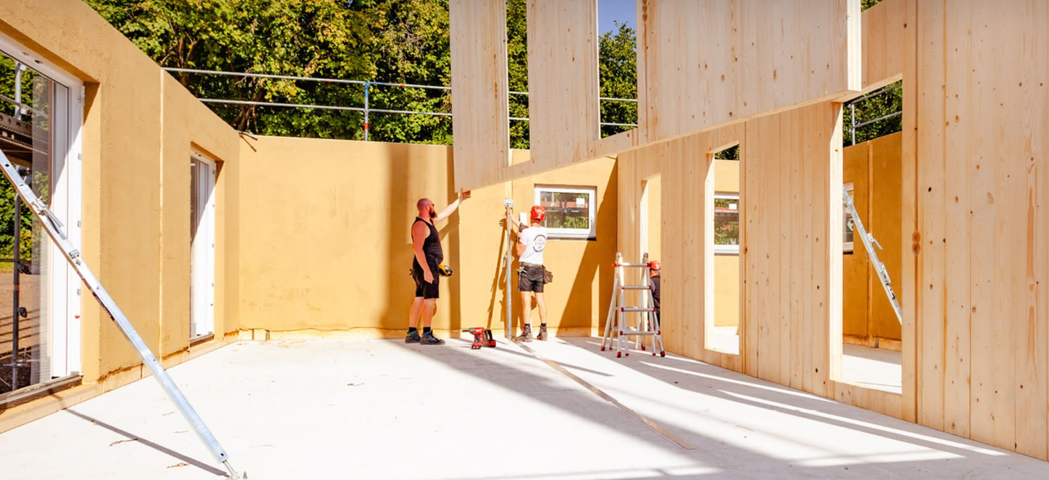 Construction workers assemble large wooden wall panels during new home construction on a sunny day.