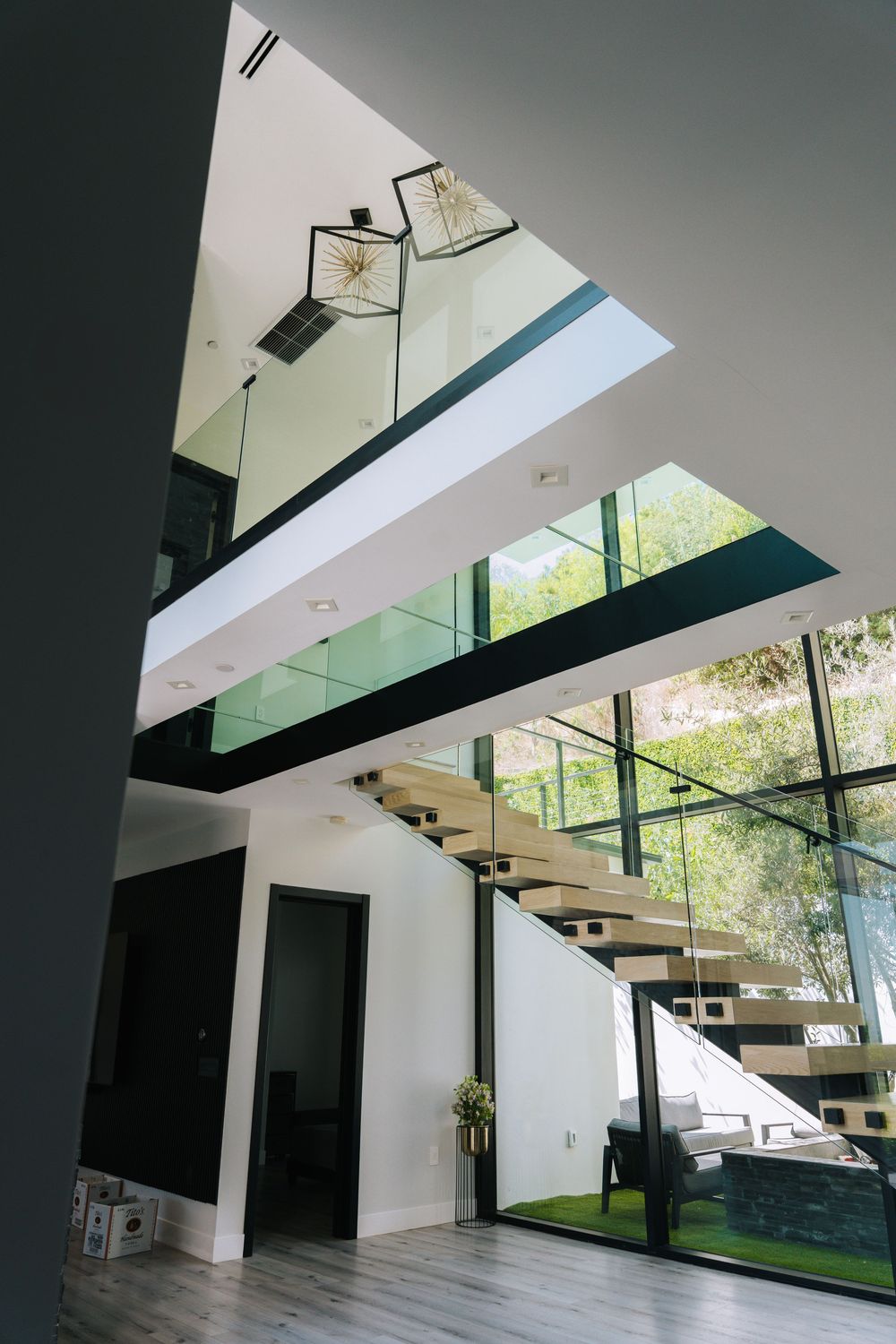 Modern floating staircase with glass panels and black accents in a contemporary white interior space with natural lighting.