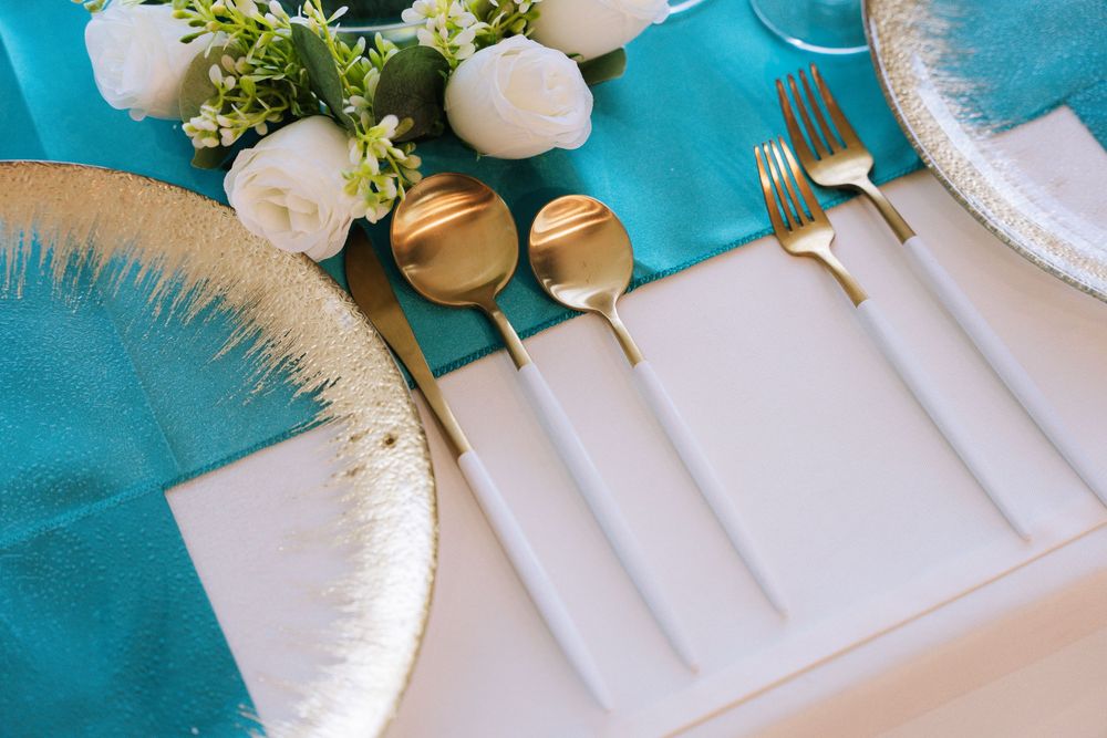 Elegant table setting with white napkins, gold cutlery, and teal blue accents for a modern wedding reception.