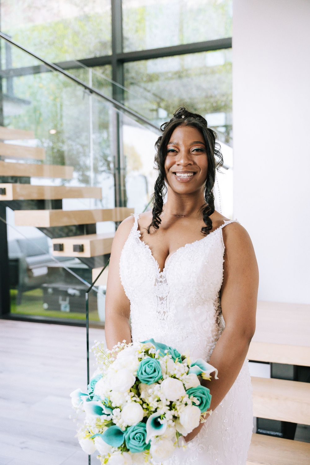 Wedding scene in bright indoor space with white dress and turquoise floral bouquet.
