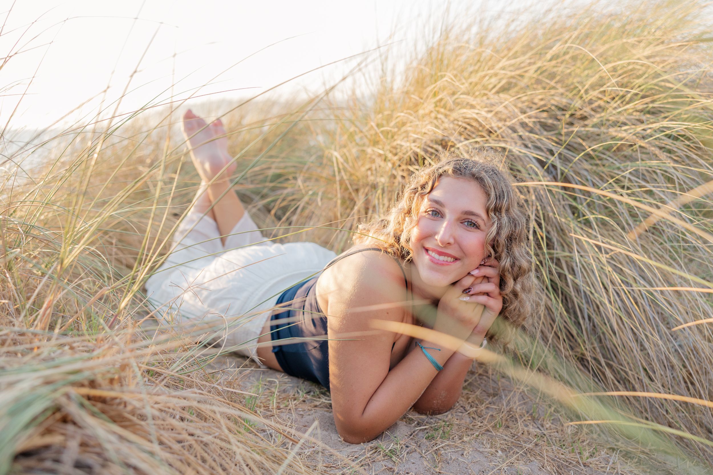 A person lies playfully in tall beige beach grass on a sunny day.